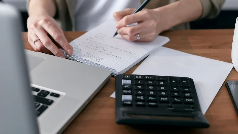 Masada hesap makinesi ve defterle bütçe hesaplayan kişi